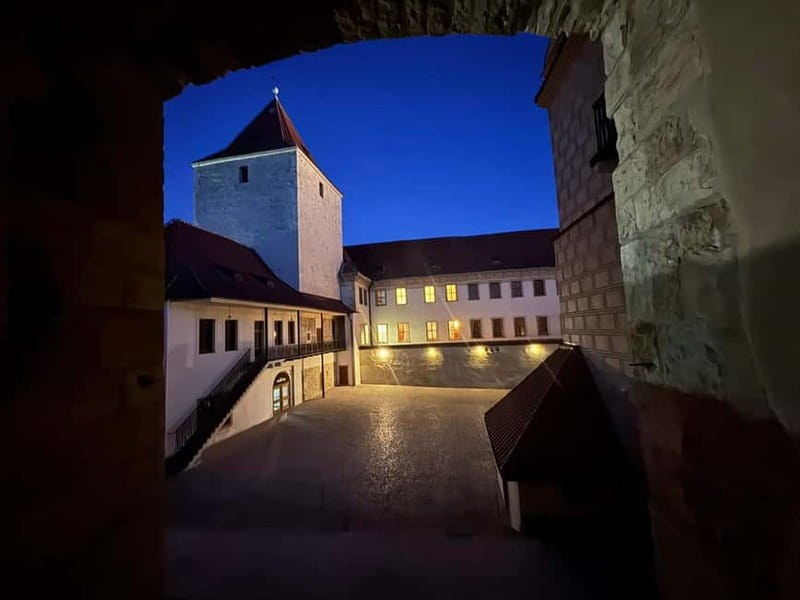 Prague: Night Walk through Prague Castle with City Views - The first castle courtyard: Rudolf II, chandeliers, and a fountain glow